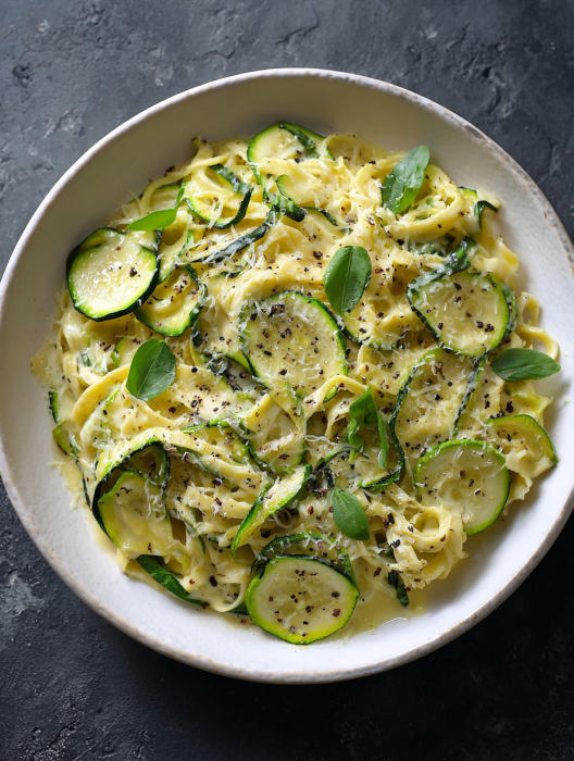 A bowl of pasta with zucchini and basil.