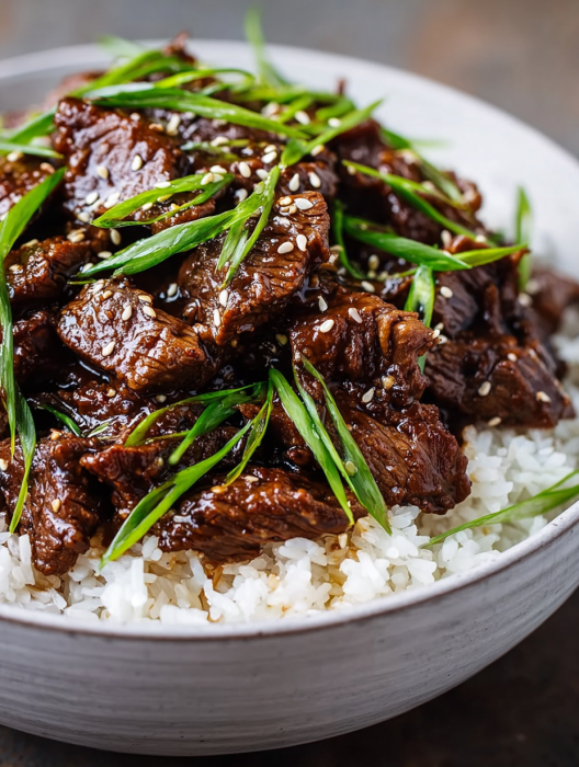 A bowl of beef with rice and green onions.