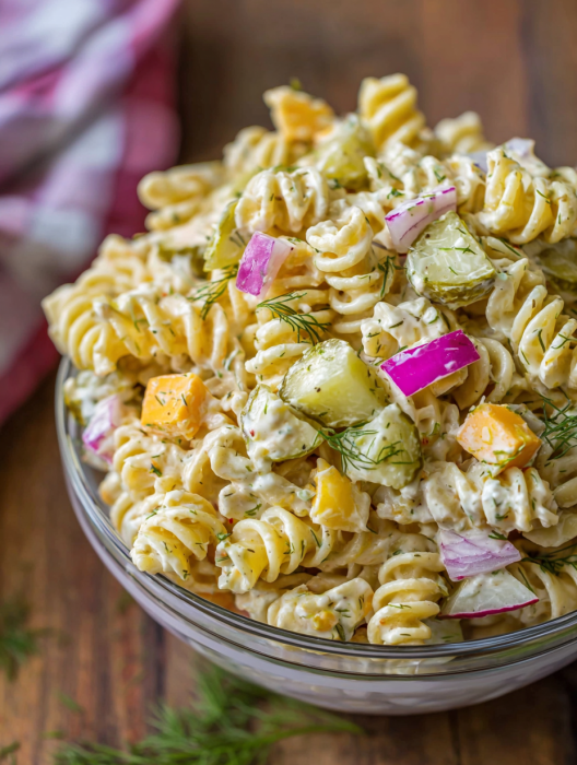 A bowl of pasta salad with dill pickles and other vegetables.