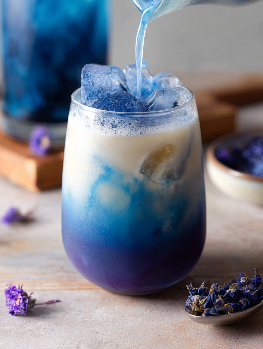 A glass of blue and purple tea with ice in it.