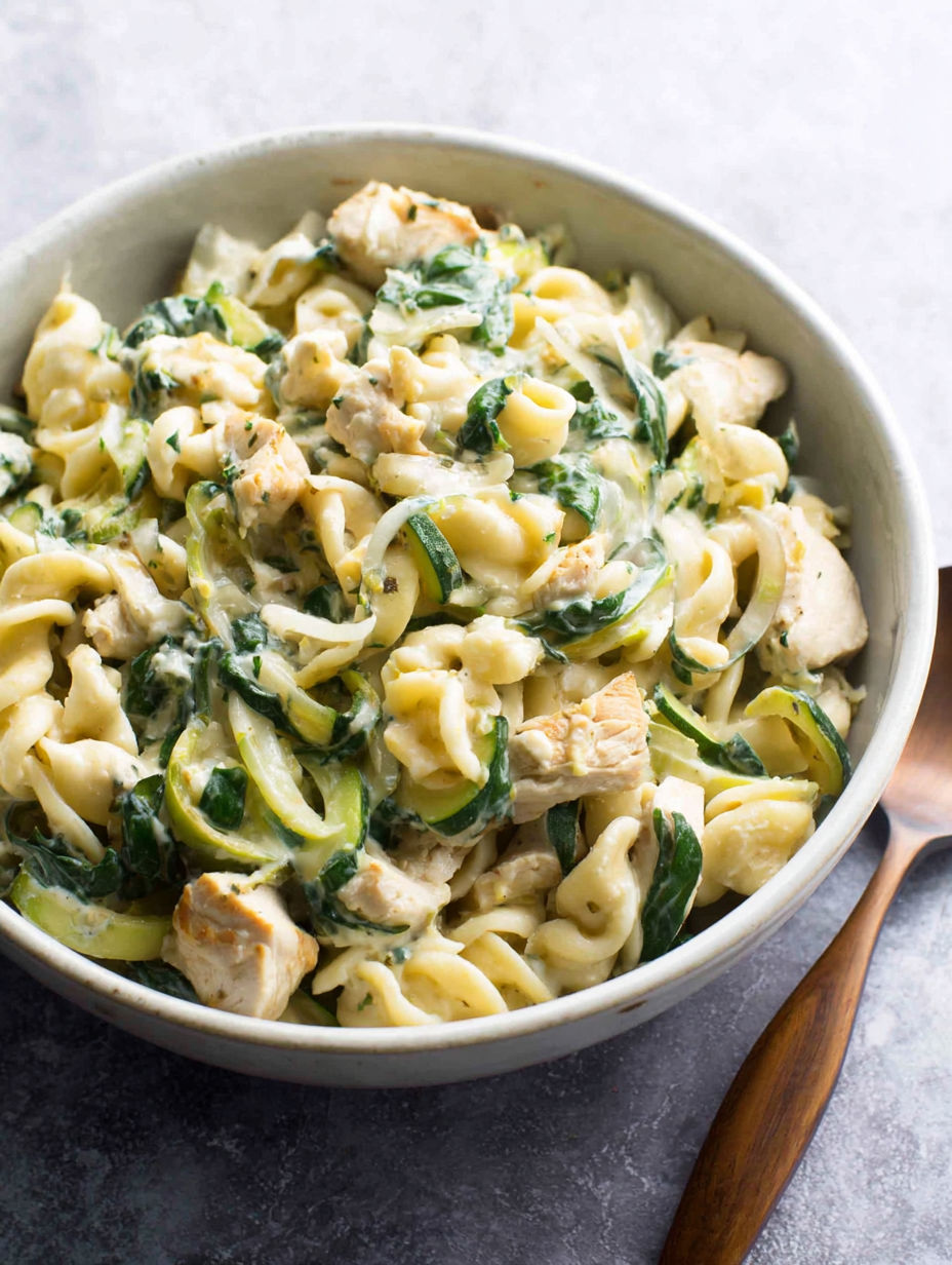 A bowl of pasta with chicken and spinach.