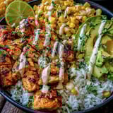 Ein Street Corn Chicken Rice Bowl mit verschiedenen Zutaten wie Avocado, Lime, Koriander, Rice, Chicken und Kartoffeln.