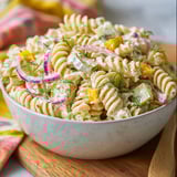 A bowl of pasta salad with dill pickles.