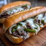 Two cheesesteak rolls on a wooden table.