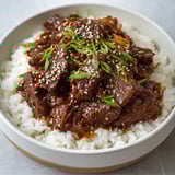A bowl of beef and rice with sesame seeds on top.