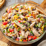 A bowl of chicken salad with corn and tomatoes.