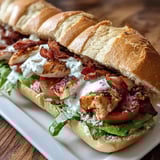 A sandwich with bacon and tomatoes on a white plate.