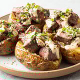 A plate of loaded baked potatoes with steak bites.