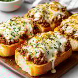 A plate of garlic bread with meat on top.