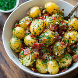 A bowl of potatoes with bacon and herbs.
