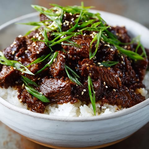 A bowl of beef with rice and green onions.