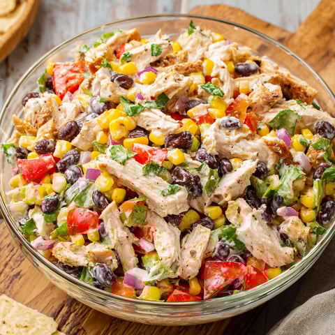 A bowl of chicken salad with corn and tomatoes.