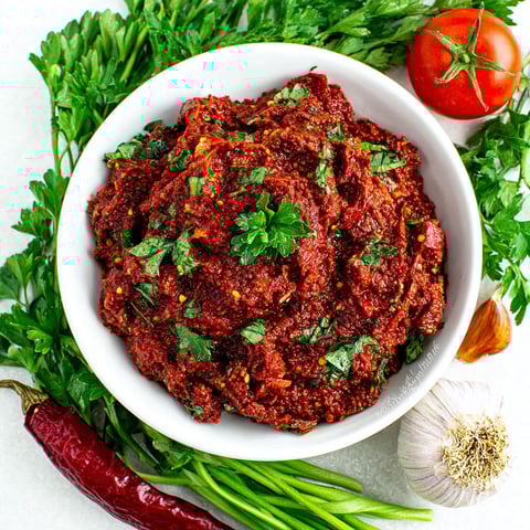A bowl of red sauce with green vegetables.