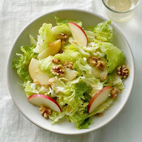 A bowl of salad with apples and walnuts.