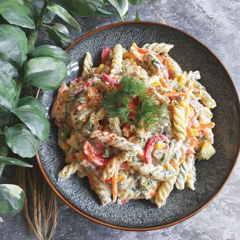 A bowl of pasta with vegetables and a sprig of parsley.