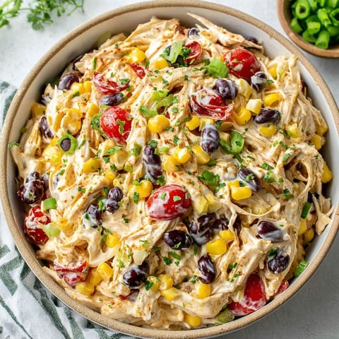 A bowl of chicken salad with tomatoes, corn, and olives.