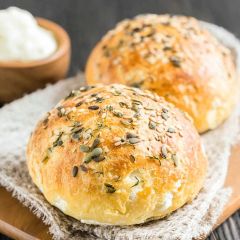Two low carb bread rolls with seeds on a wooden board.